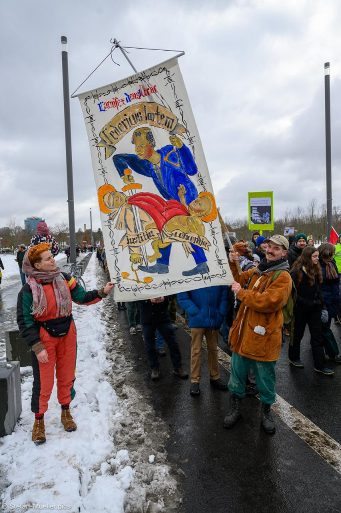 Mann mit Schild: „Carnifex deus uberior = CDU Fredericus Martem justitia concordia“. Auf dem Schild ermordet Merz mit einem Schwert Justitia, die Göttin der Gerechtigkeit, und Concordia, Göttin der Eintracht. Beim Klimastreik von Fridays for Future vor der Bundestagswahl 2025, Wilhelmstraße, Berlin, 14.02.2025