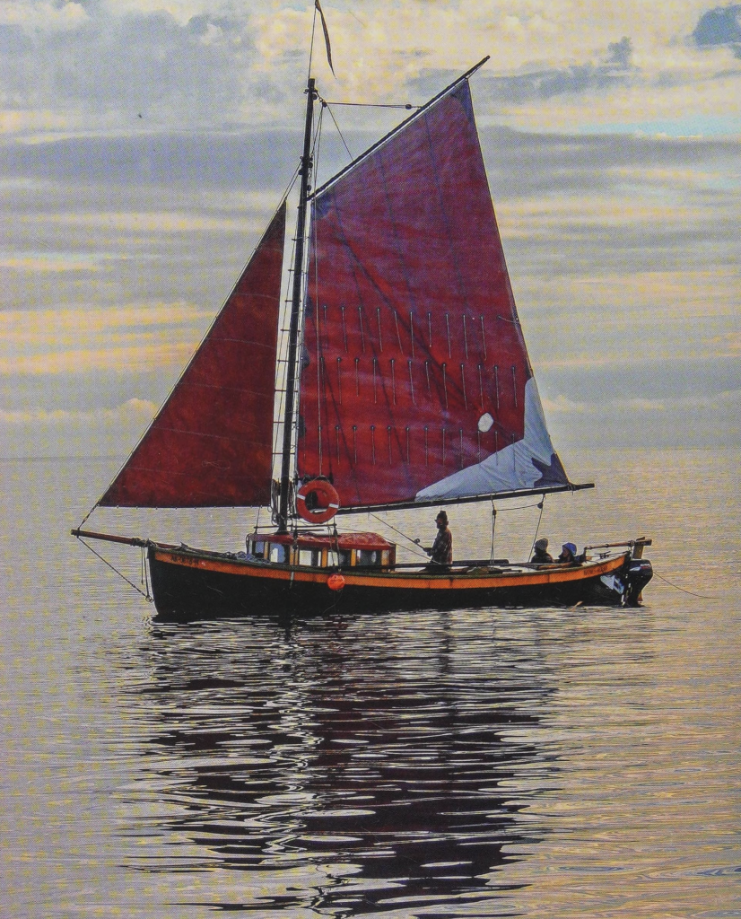 A small, single masted sailboat with deep red sails raised. Three people are onboard. Surely there's room for a few more?