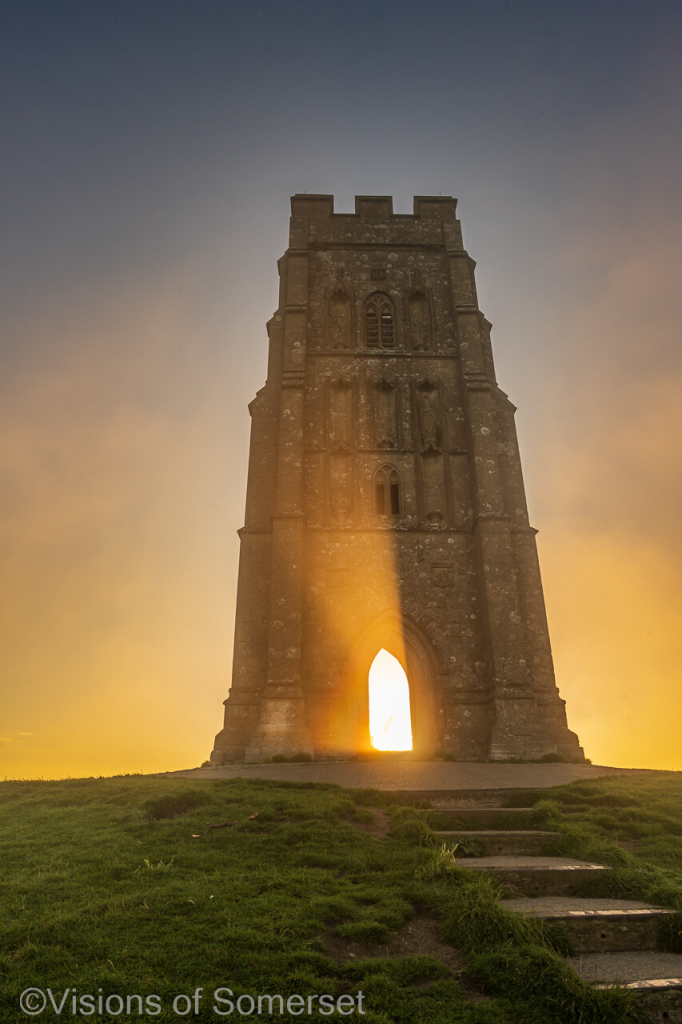 A beam of light shining through the mist in the archway of the tower which dominates the scene.