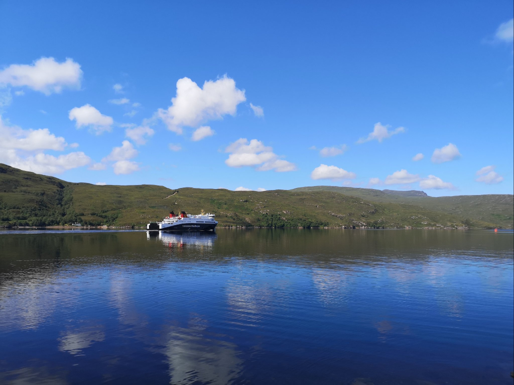 Die Fähre von Ullapool nach Stornoway verlässt den Hafen Ullapool und fährt durch das Loch Broom in Richtung äußere Hebriden.
Die Fähre ist unten schwarz und oben weiß gestrichen.
Im Hintergrund fährt sie an einer Hügelkette entlang