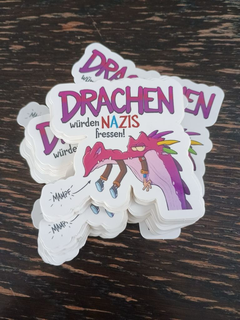 Sticker mit der azfschrift drachen würden nazis fressen. Ein rosa cartoon drache hat einen nazi im mund. Man sieht nur noch beine und arme