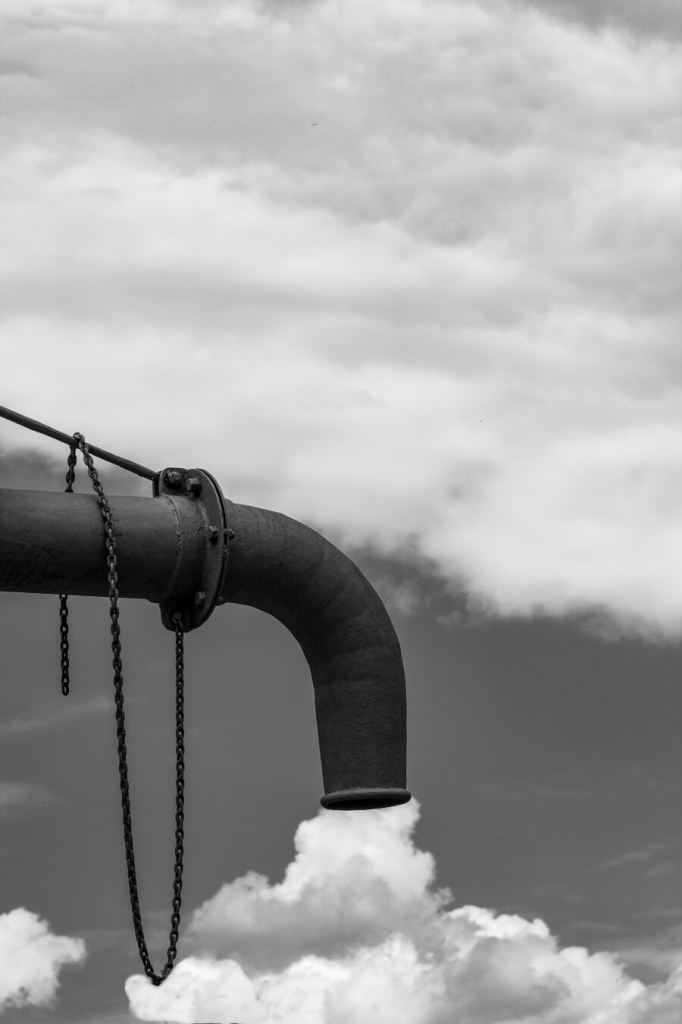 Black and white photograph showing a steel pipe surrounded by clouds and it seems as if part of those clouds were smoke coming out of that pipe