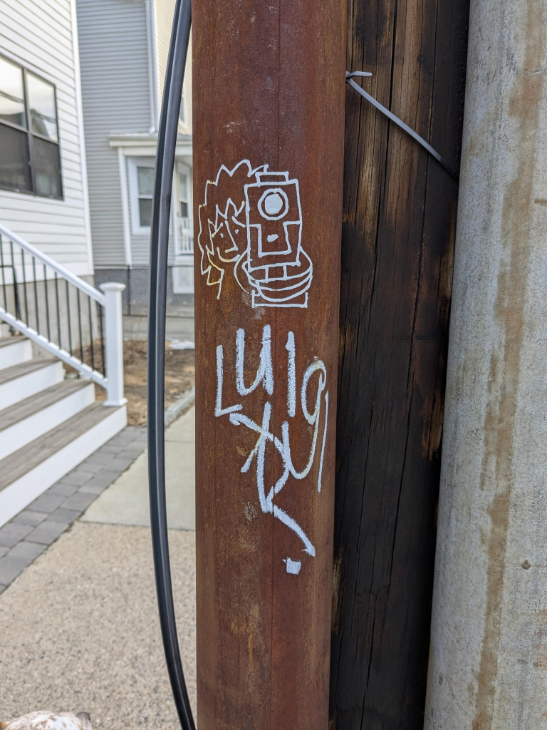 Graffiti in silver paint pen  showing a man pointing a pistol at the viewer, and underneath is the name "Luigi"