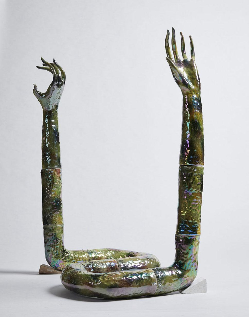 Sculpture of a scaly snake form with a shiny green glaze, with each end turning into an outstretched hand outstretched vertically.