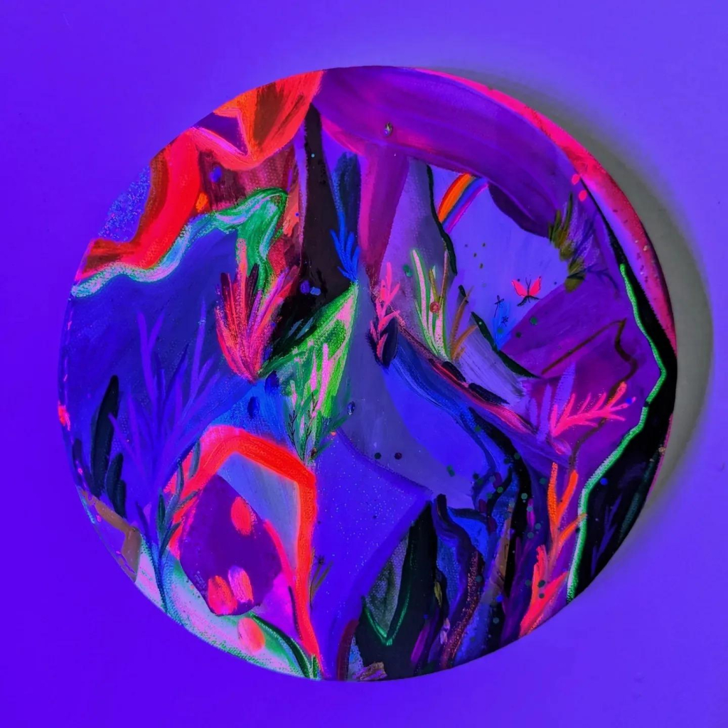 Abstract all-over painting on a circular canvas with colorful gestural strokes, shown under a blacklight revealing hot pink and bright green shapes against dark blue and purple.