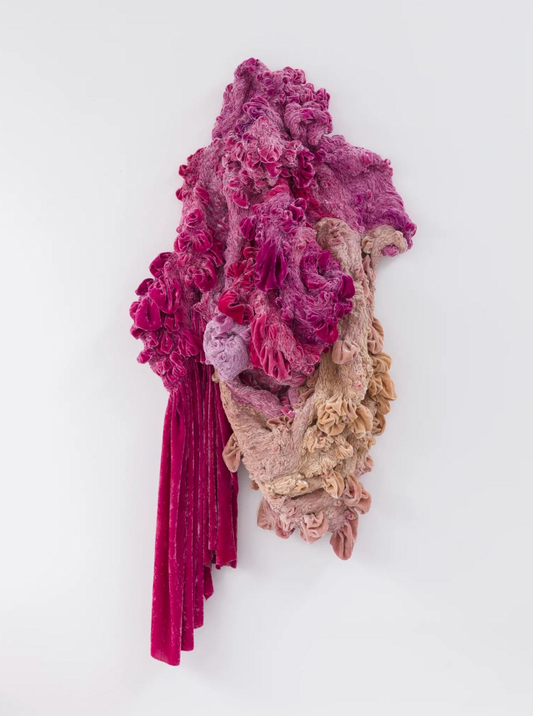 Hanging wall sculpture of combined magenta and cream fabrics folded and stitched into an abstract organic form.