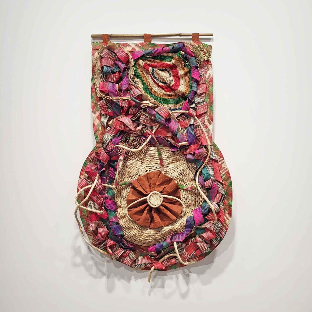 Hanging sculpture of woven basket forms and multicolor curling ribbons encircling a central circular form in orange.