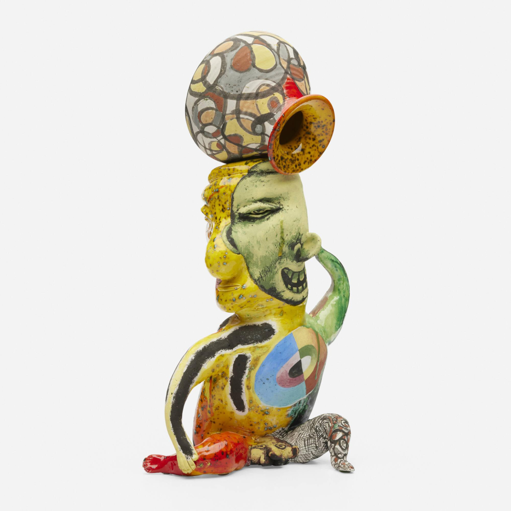 Ceramic sculpture of an abstract figure painted in bright colors, balancing a patterned vessel atop their head.