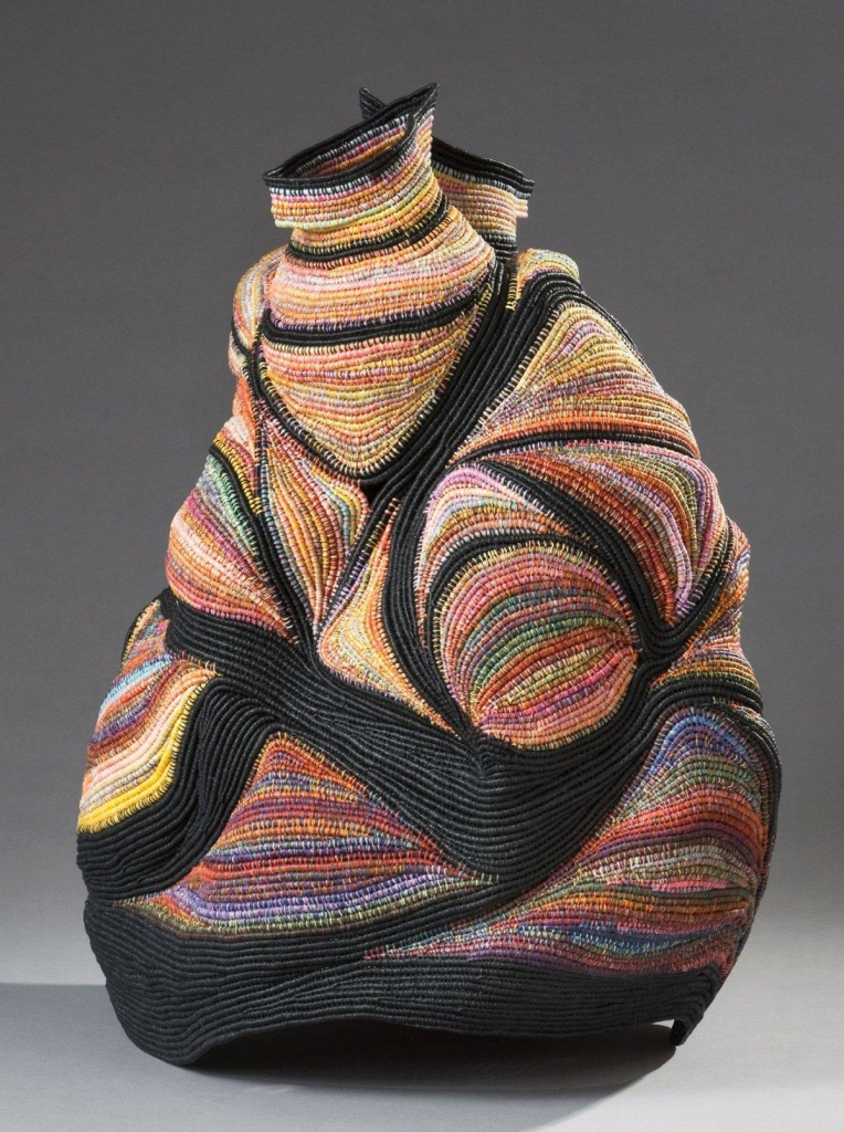 Abstract sculpture of a textured, rounded, bulbous vessel with two small round openings on top, made up of multicolor coiled threads with bold sections of black curving throughout.