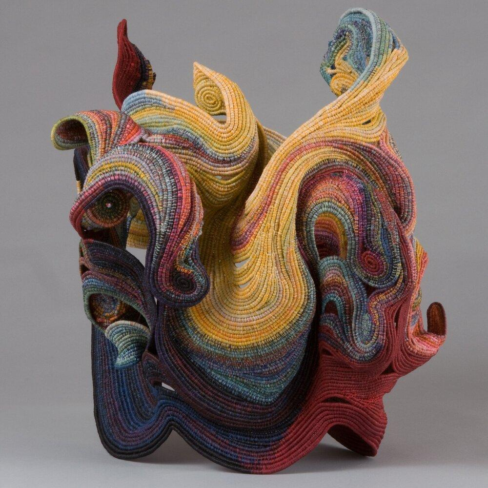 Abstract sculpture with curving edges swirling around and jutting outwards, made up of multicolor coiled threads.