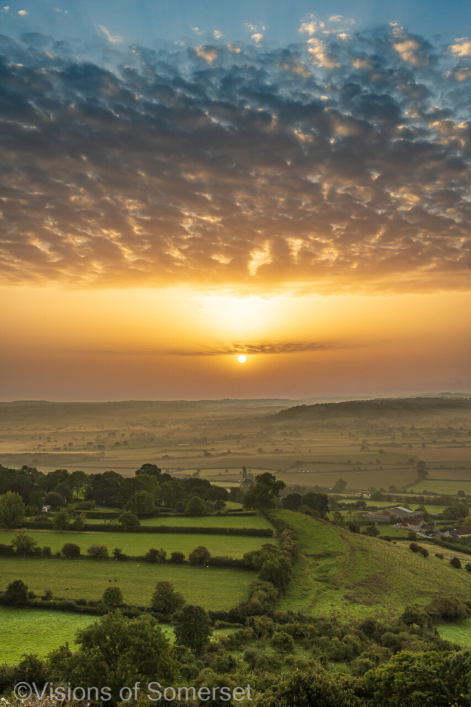 A fan of golden cloud with hints of blue above. Land below. The sun is hazy.