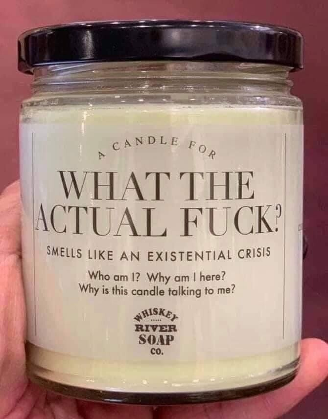 photo of a hand holding a candle with a label that says: a candle for What the Actual Fuck? Smells like an existential crisis - Who am I? Why am I here? Why is this candle talking to me? Whisky River Soap Co.