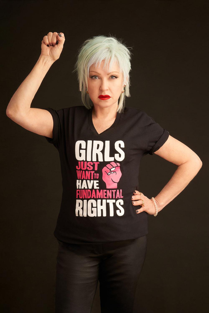 Cyndi Lauper wearing a "Girls just want to have fundamental rights" t-shirt with a red fist while making a fist salute