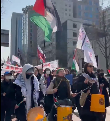 Protesters in Seoul led by drummers, carrying placards, banners and a large Palestinian flag.