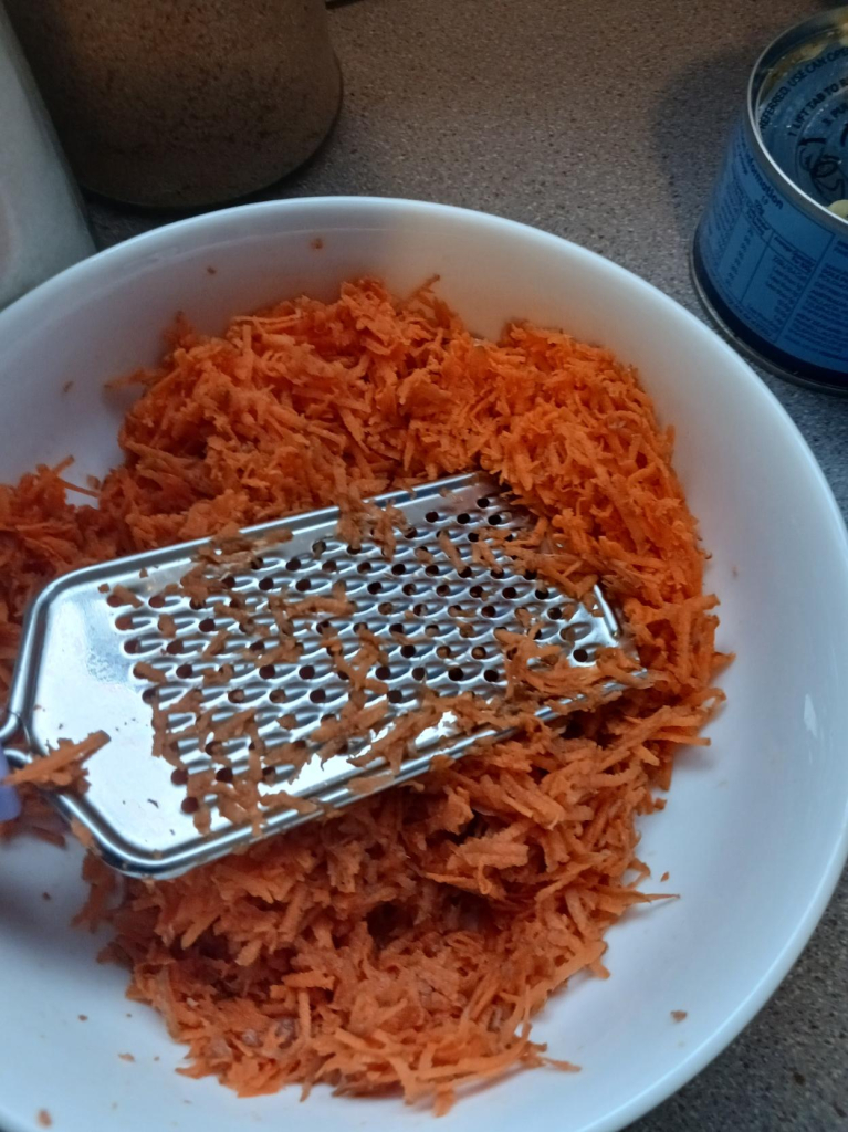 grated carrots and a grater in a white bowl