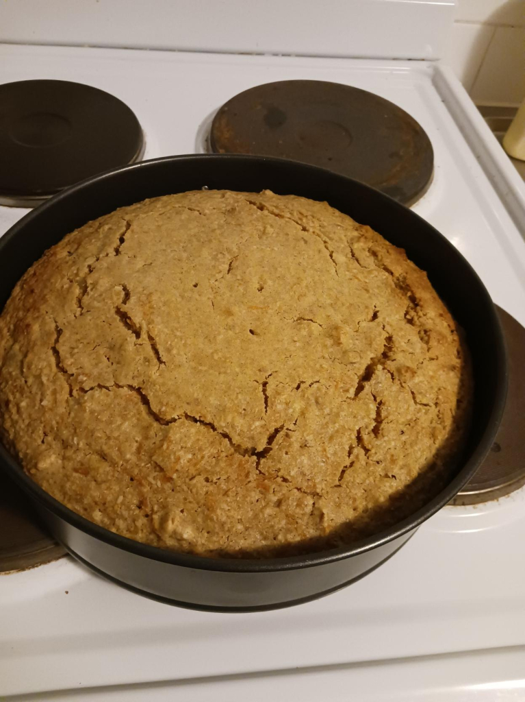 the carrot cake i just pulled out of the oven, in a round tin, sitting on the stove