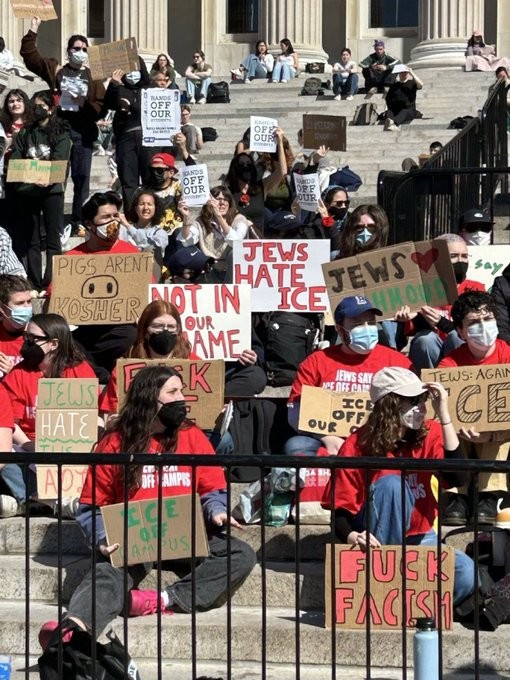 Groups of students sitting on the steps of a building holding placards reading
PIGS AREN'T KOSHER
JEWS HATE ICE
ICE OFF OUR CAMPUS
JEWS 💖MAHMOUD