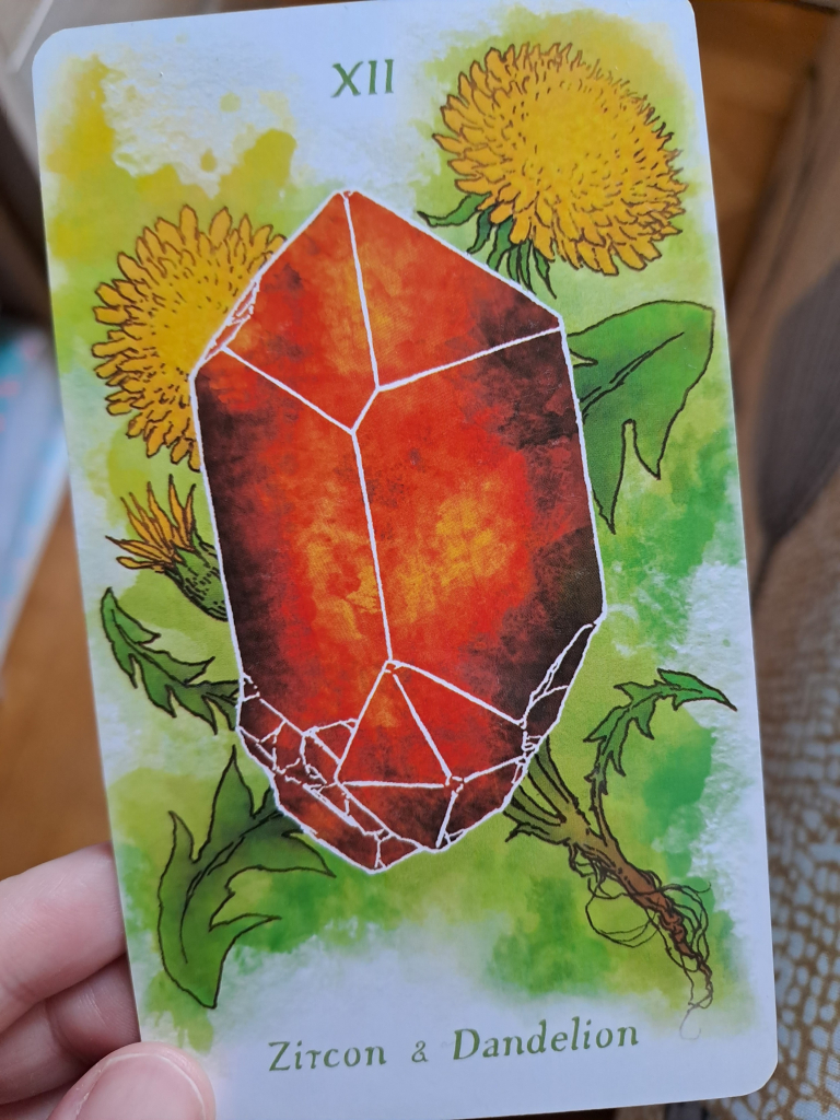 Watercolor tarot card showing an orange colored zircon crystal against a background of dandelions.