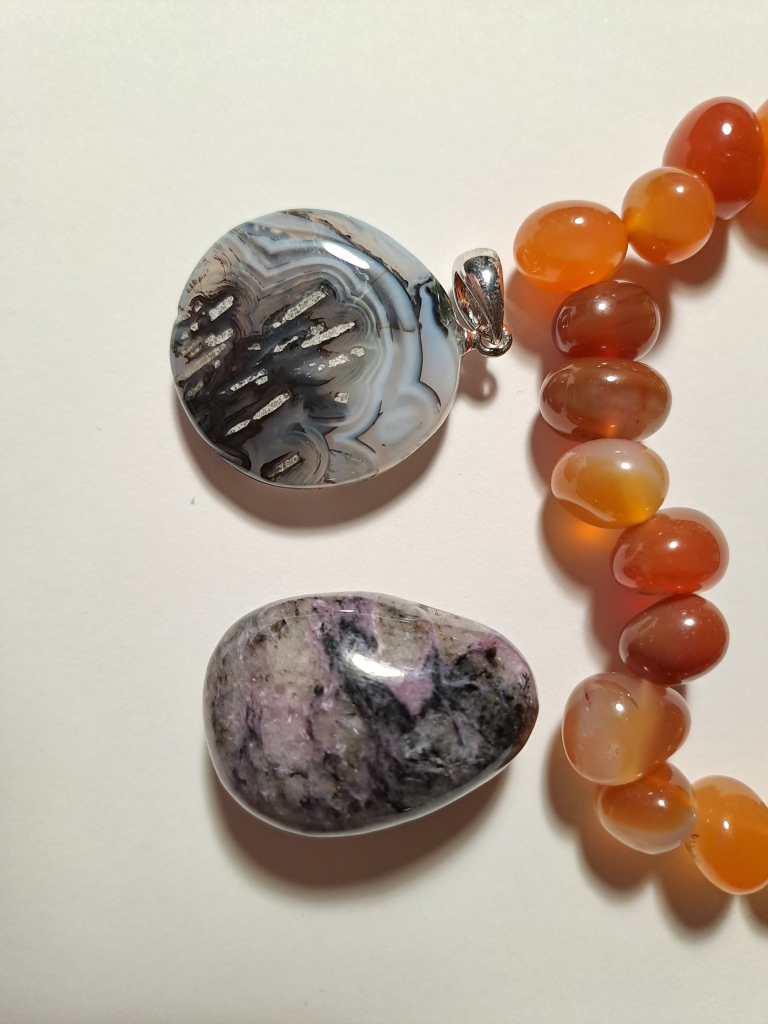 Close up of the two pendants, showing the back of the agate pendantwithwhite, black, and translucent stripes.