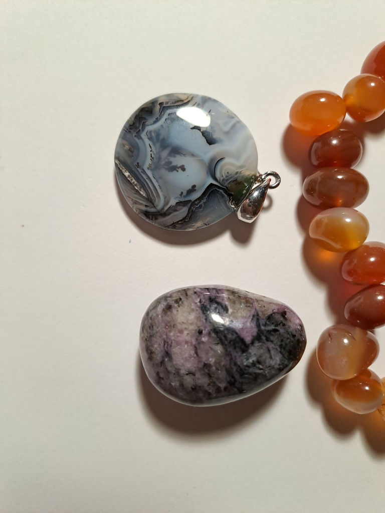 Close up of the two pendants, showing the front of the agate pendant with dendrite features. Part of the orange carnelian bracelet also visible.