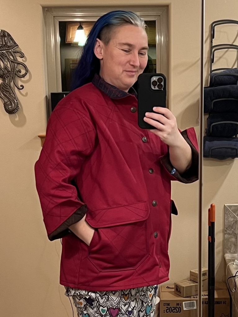 Mirror selfie of me in the red jacket. I have one hand in a side seam pocket and I’m smiling at the camera. 