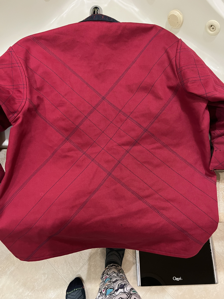 The back of the red jacket, one last time. It’s quilted in indigo with a large X that crosses in the middle of the back. Each arm of the X is made of up parallel lines of different stitch lengths. It looks like minimalist Xmas plaid. 