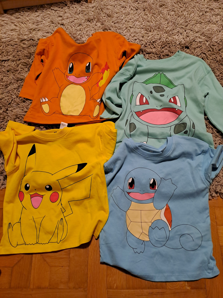 A photo of four childsize longsleeve shirts, one with Pikachu, one with Charmander, one with Bulbasaur and one with Squirtle