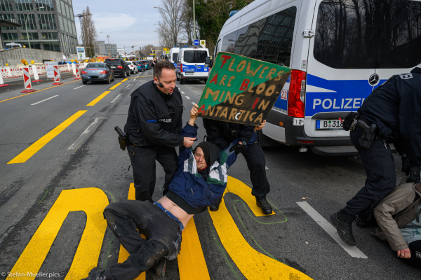 Polizei versucht die Straßenblockade durch Klimabündnis zu verhindern. Aktivist hat Schild, auf dem steht: „Flowers are blooming in Antarctica“, Elsenbrücke, Berlin, 02.03.2024