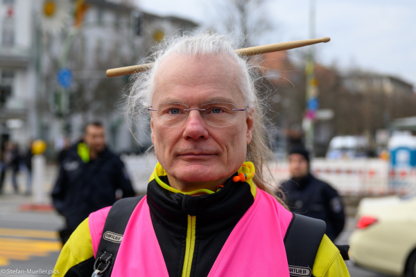 Edmund Schultz von den XR drummers mit Schlagzeugstock in den Haaren bei der Blockade der Elsenbrücke, im Hintergrund zwei Polizisten, Berlin, 02.03.2024