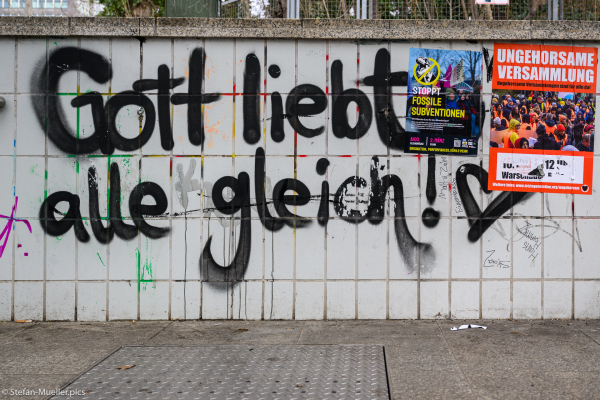 Graffito „Gott liebt alle gleich!“ und Plakate der Klimagerechtigkeitsbewegung, dem Bündnis „Stoppt fossile Subventionen“ und „Letzte Generation“, Berlin, 02.03.2024