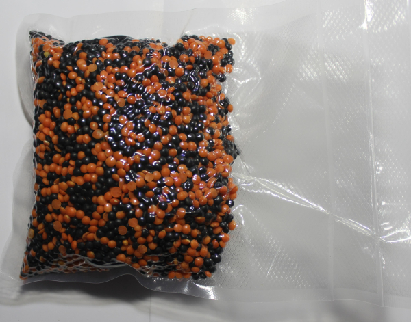 A vacuum sealed bag, half-filled with red lentils and black beans. An electronic device is presumably hidden within the lentil-bean mixture within another plastic bag.