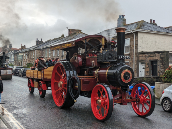 A red steam traction engine travelling down a street. 