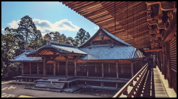 A view of one of the buildings of the Engyoji complex seen on the left from the 2nd storey wooden balcony with the balcony and underside of the overhanging roof wood going into the distance on the right