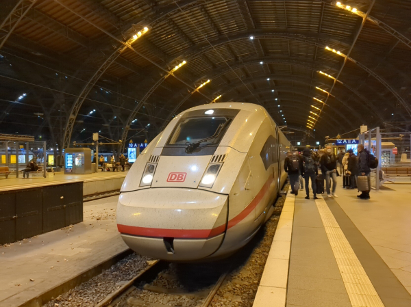 The train arrived at the platform, front/diagonal view. Leipzig hbf is a series of cavernous, steel-frame arches with yellowish lighting.