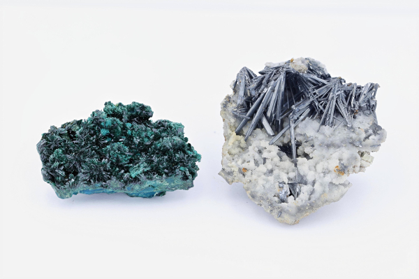 On the left, deep blue-green crystals growing in a dense, mossy pattern. On the right, fuzzy white crystals topped with shiny dark grey crystals, together resembling a pile of mechanical pencil lead dropped onto a carpet.