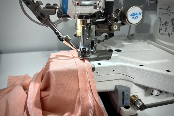 Binding being sewn onto the collar of a peach t-shirt using an industrial coverstitch machine.