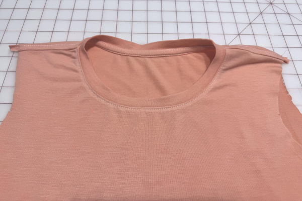 Exterior front view of a peach t-shirt with binding sewn on the collar after a successful second pass.