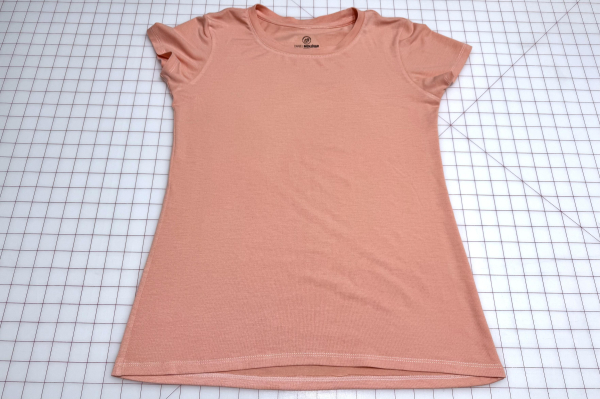 Front exterior view of a freshly sewn peach jersey t-shirt laying flat on a large cutting mat.