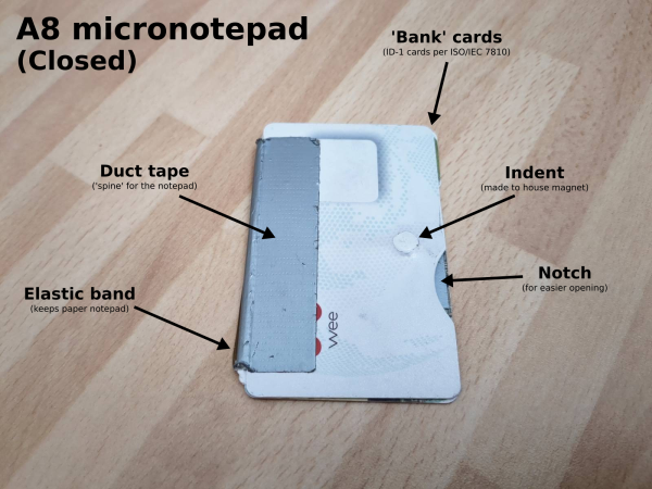 A mostly white bank card on a wood veneer table. A piece of silver duct tape is visible on the left side, joining it to another bank card behind. A notch is cur out at the right hand side, and an indent is visible into which a magnet is recessed.