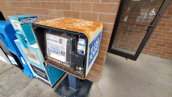 Rusty and run down newspaper machines in front of a public building. 