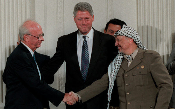 Bill Clinton behind PLO leader Yasser Arafat and Israeli PM Yitzhak Rabin shaking hands, in the white house.