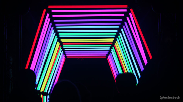 A photo of the tunnel entrance. The frame is black, and there is an angular archway of rainbow coloured stripes. At the bottom the black includes the silhouettes of some of the visitors heads and shoulders.