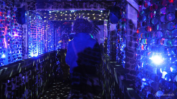 Photo inside the bridge across the loch, lit up in blue. There is a glitter ball in the centre flinging dots of light all around, and the walls are strings of circled mirrors. There are some people walking through.