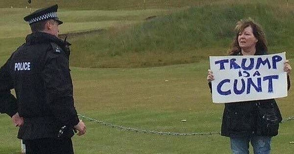 Janey Godley holding a sign which says "Trump is a cunt" as a policeman watches.