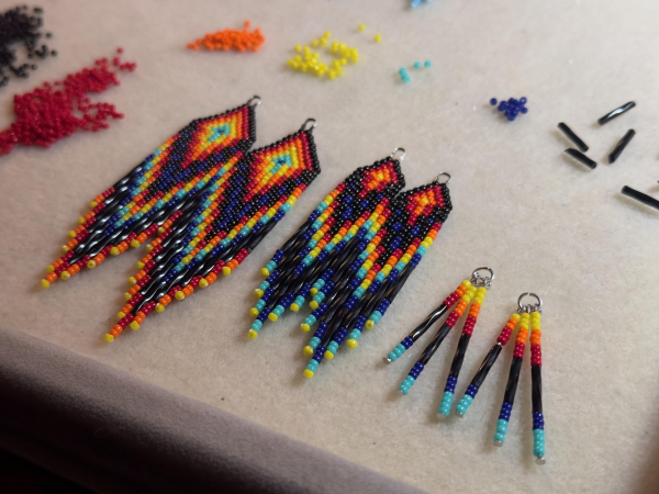 Three pairs of black, red, orange, yellow, and blue beaded earrings on a bead mat