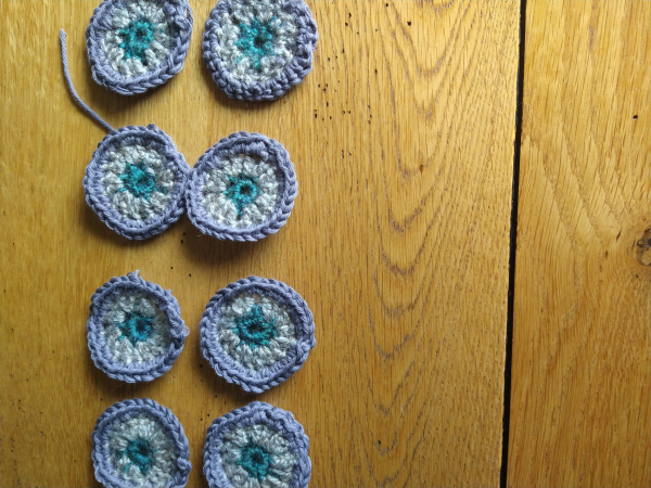 Eight small crochet circles, with a green centre, mushroom round two and then a slate grey outer, they will form part of a larger crochet Afghan blanket 