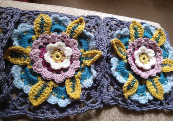 Two Legacy motif crochet squares.  Pink, blue and white multi coloured flower in a grey lacy square 