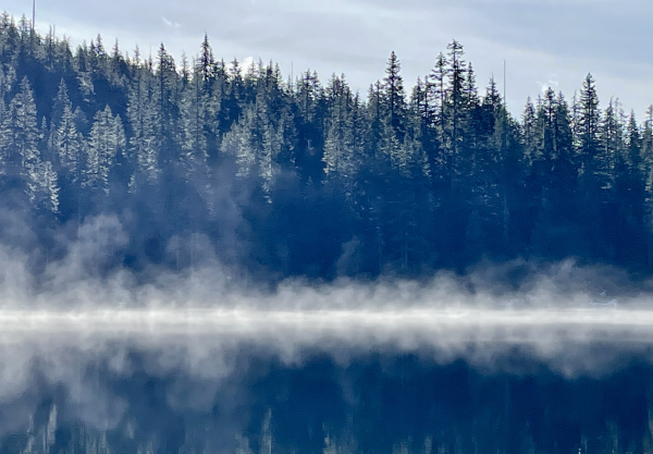  Mist rising off a dark blue clear mountain lake ringed with tall green trees dusted with snow.  Ollalie Lake in the central cascades. 