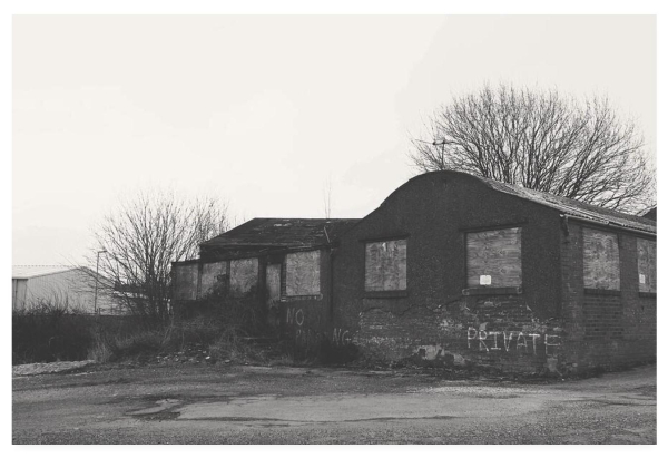 Gloomy black and white photograph showing a boarded up building on an English industrial estate.