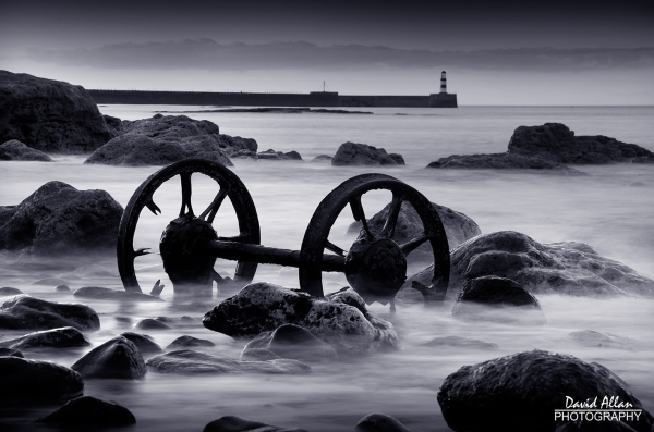 Industrial heritage, in the form of a set of old iron wagon wheels, resting on a rocky inter-tidal zone of a Durham beach at Seaham in North East England.